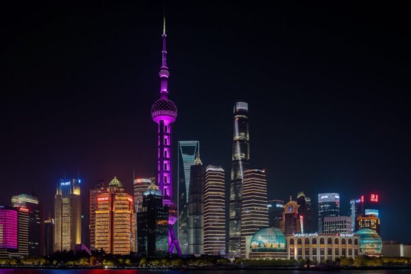 A panoramic view of the Shanghai skyline featuring the Oriental Pearl Tower, modern skyscrapers, and the Huangpu River during nighttime.